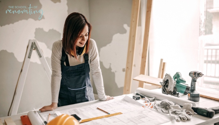 Female renovator reviewing renovation plans and managing contractors confidently at a workbench.
