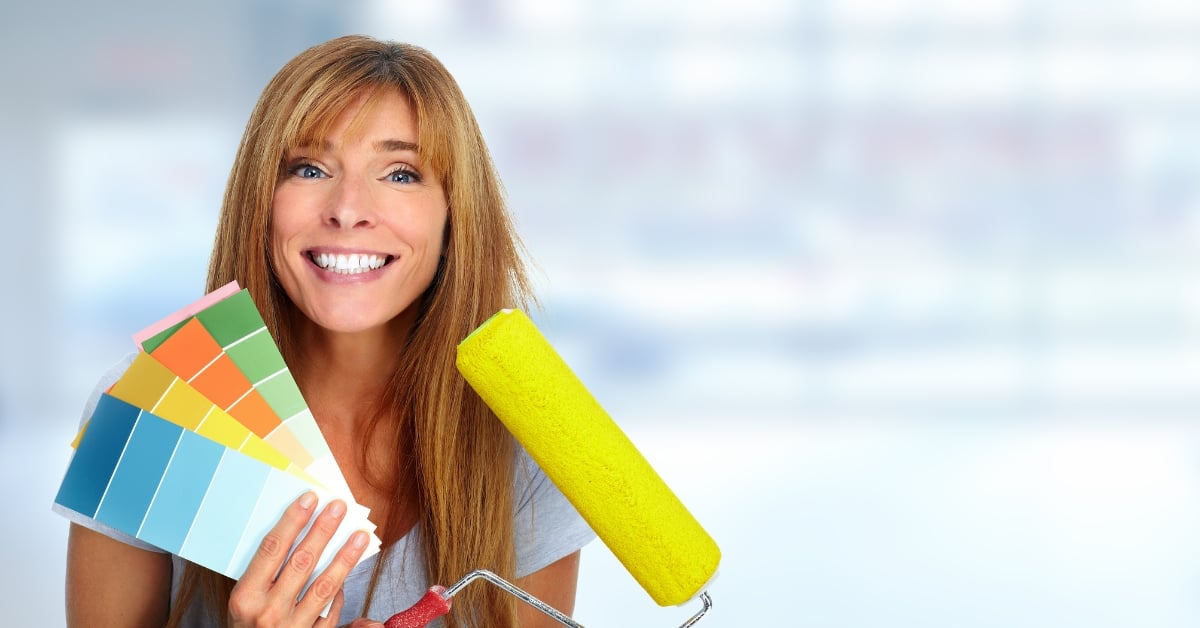 Smiling woman holding a paint roller and color swatches, illustrating active retirement planning for women over 50 through renovation.