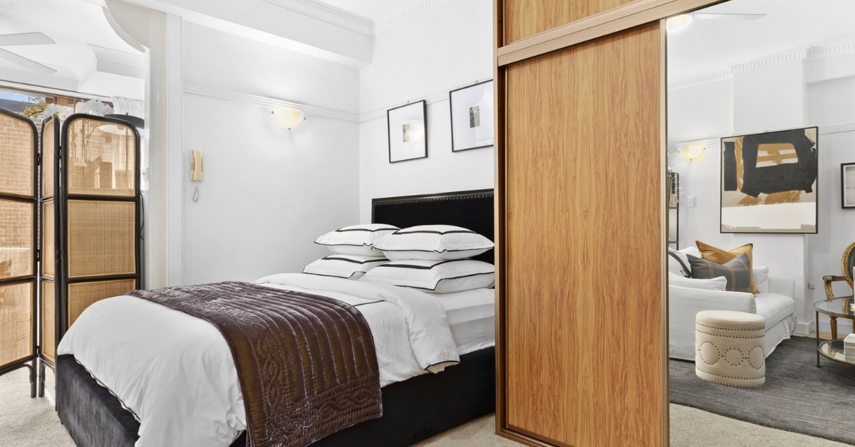 A beautifully styled small bedroom featuring a wooden sliding partition and rattan room divider, demonstrating how to maximize space for student accommodation or profitable room renting.