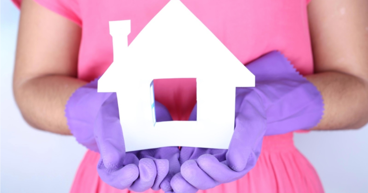 Woman wearing purple renovation gloves holding a white paper house model, symbolizing how to eliminate your mortgage with renovation strategies.