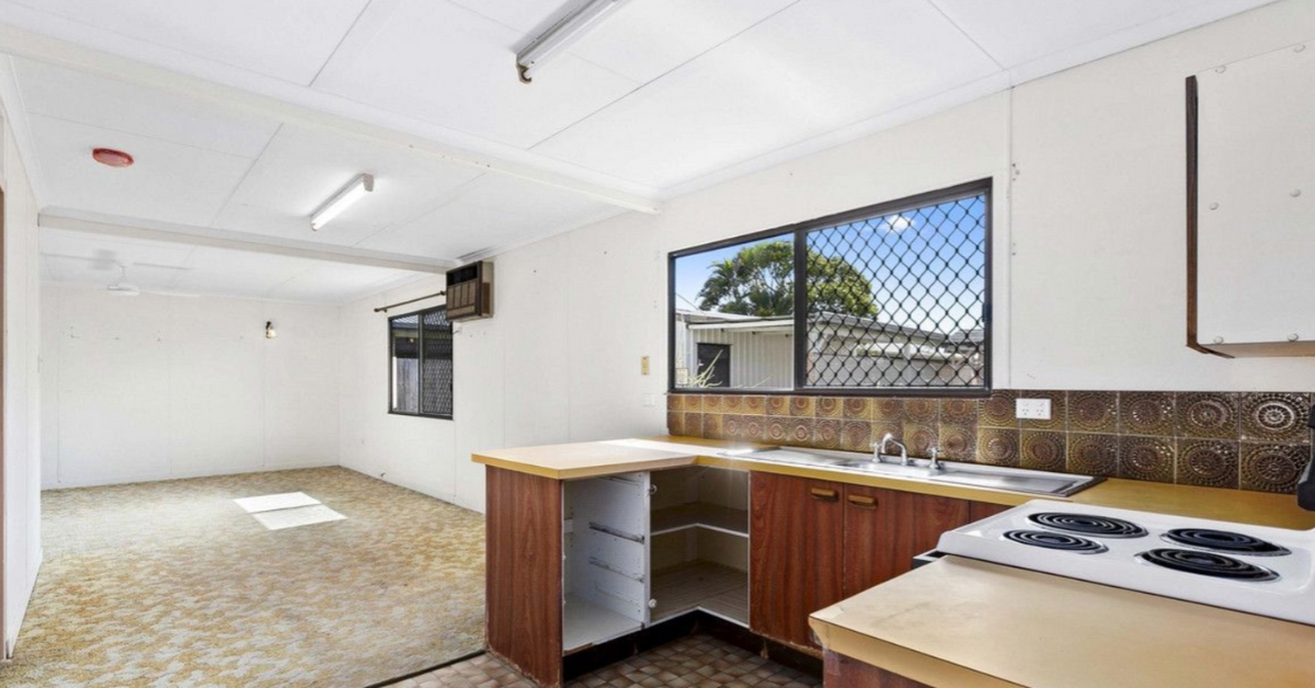 A dated, unrenovated kitchen with brown cabinets, yellow countertops, and retro linoleum flooring, illustrating a raw property project where renovation systems and trade due diligence are critical.