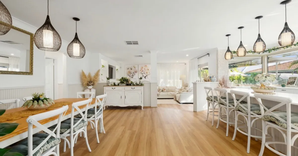 Renovated open-plan kitchen and dining room with timber floors, white cross-back chairs and black wire pendant lights