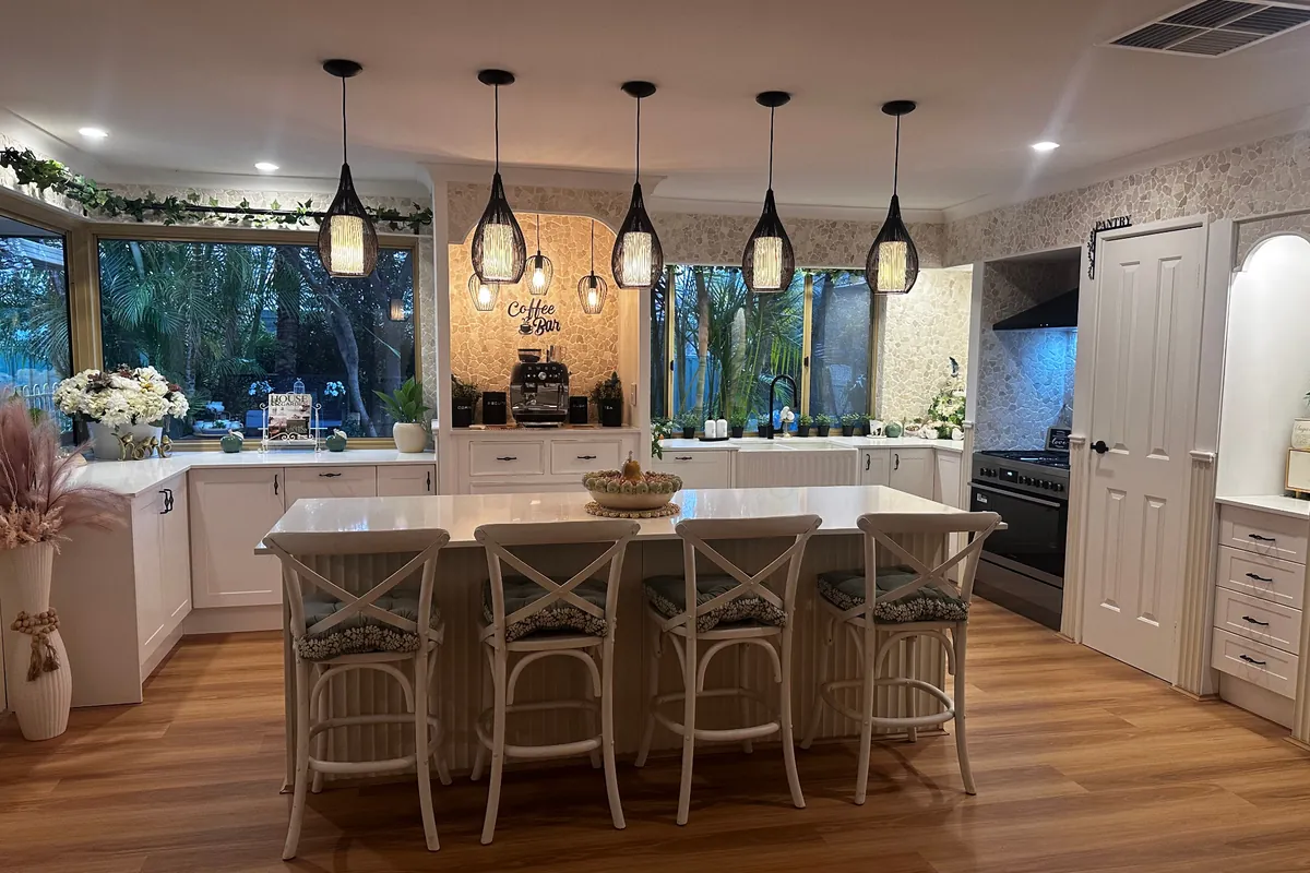 Renovated white kitchen with a stone-topped island, four cross-back bar stools, black pendant lights and an arched coffee bar